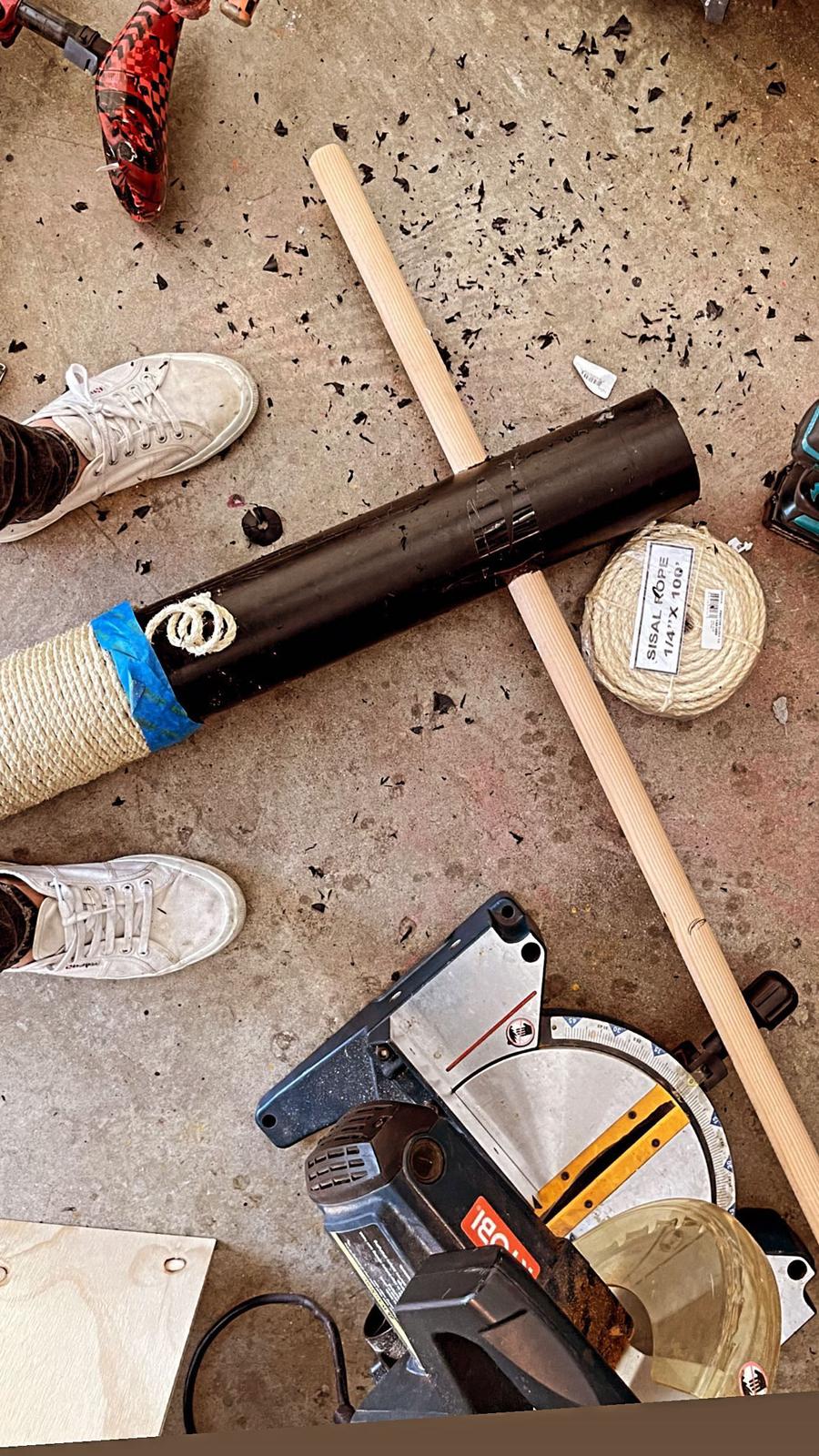 The pipe in the workshop next to a wooden dowel, a roll of jute rope, and a miter saw.
