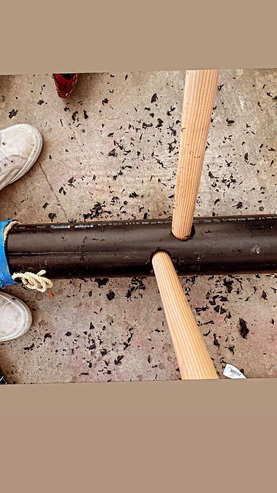 The PVC pipe on the workshop floor with two wooden dowels driven through it forming a crossbar.